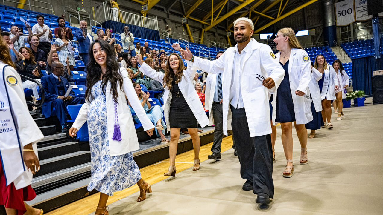 Students in white coats walking at the 2025 pinning ceremony