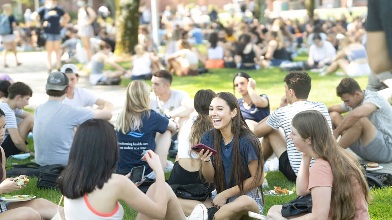 Students sit in groups on the lawn as they eat lunch and talk