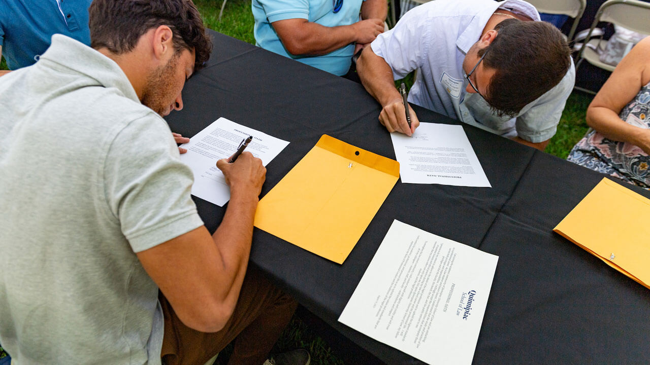 Students signing of papers on blue clothed tables