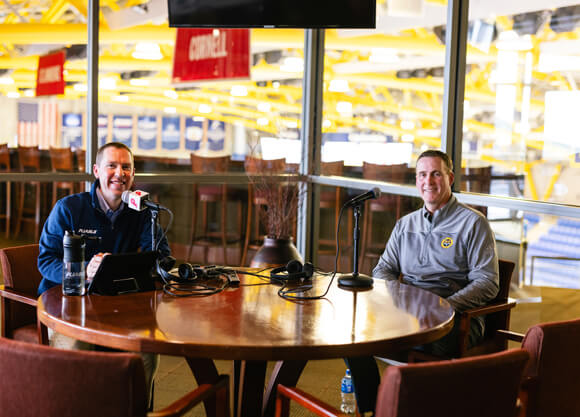 Greg Glynn, founder of Pliable, sits with Rand Pecknold at a table with recording equipment