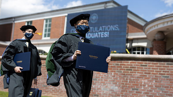 A medical school graduate holds their diploma as they walk off stage