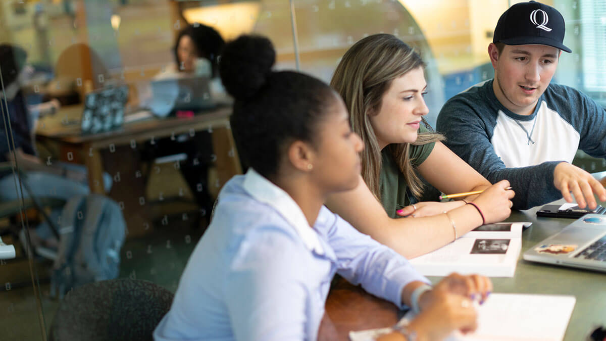 A group of students sit at a table in the library studying