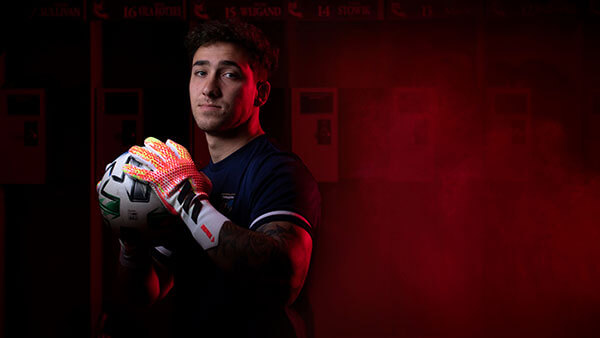 Jared Mazzola stands in his soccer uniform holding a soccer ball.