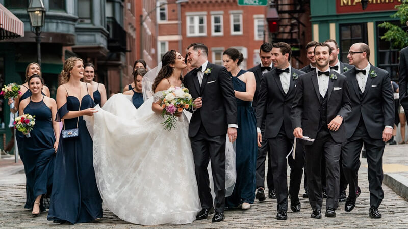 Erik and Paige Benotti surrounded by their wedding party on their wedding day kiss on a city street