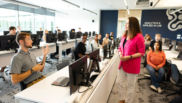 Dozens of students and professor talk in the Applied Analytics and AI Lab classroom
