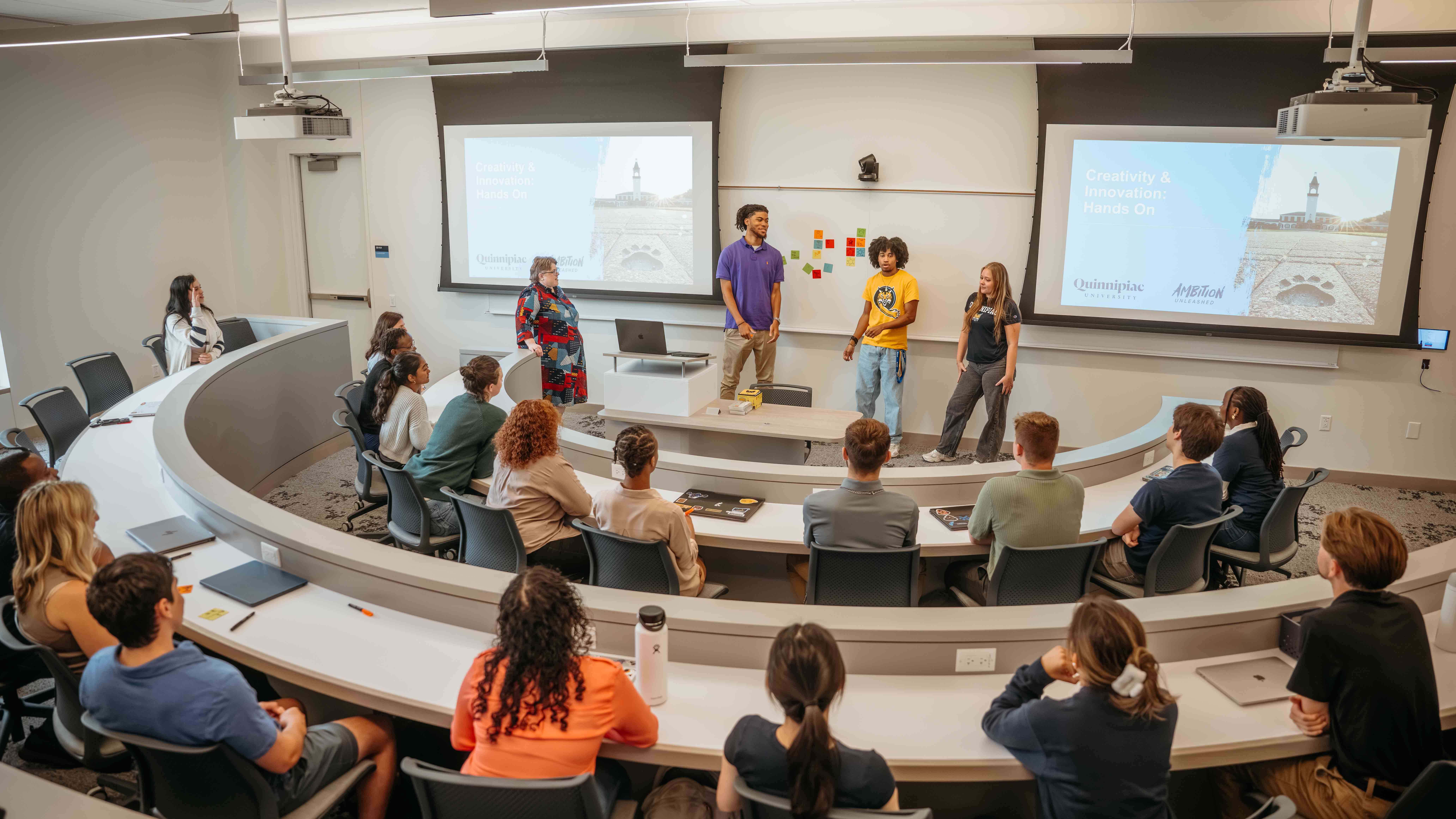 Three students give a presentation to a full classroom in the School of Business.