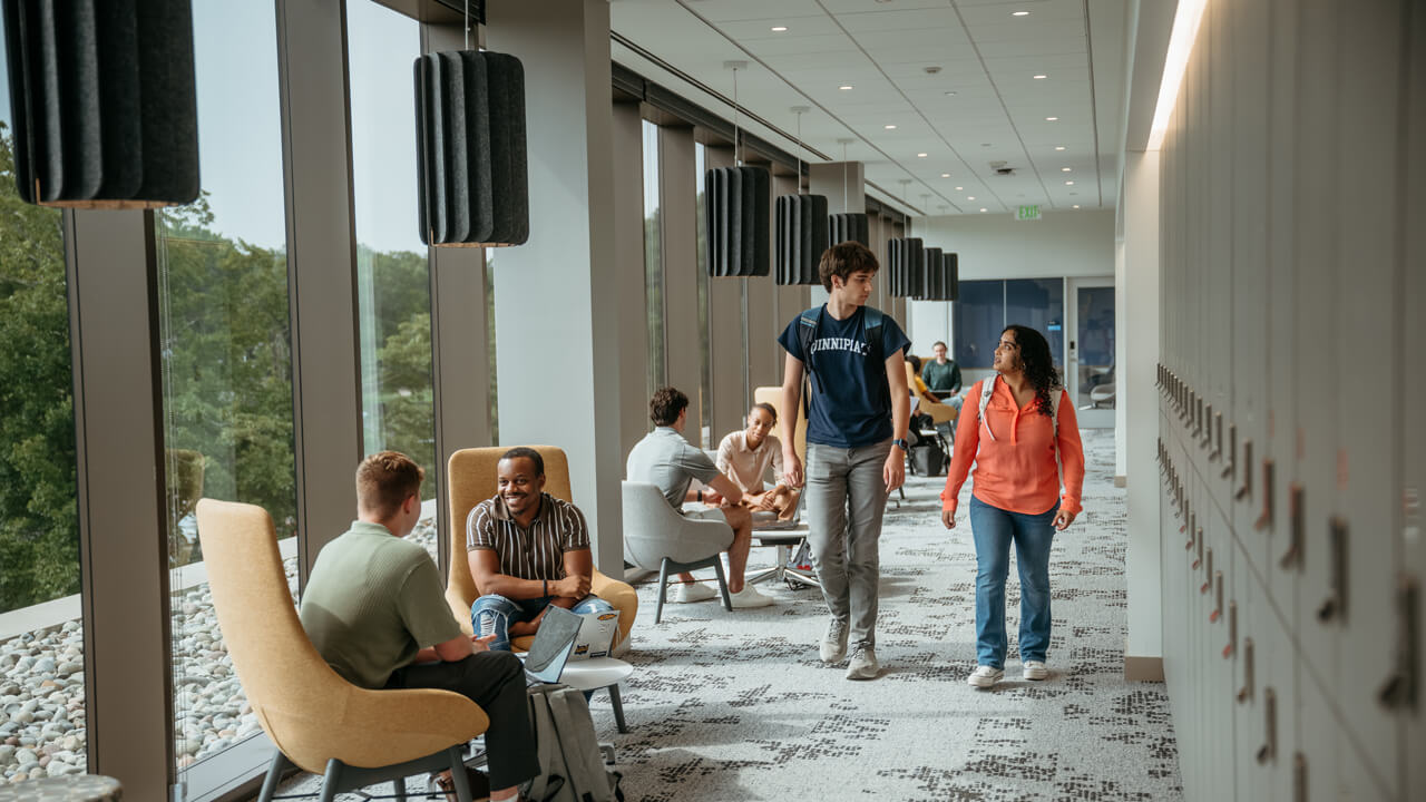 Two students walk through the Graduate Student lounge, busy with students conversing and collaborating in the area.
