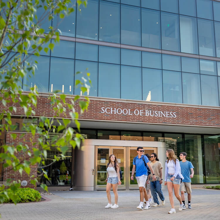 Quinnipiac students walking across the South Quad with the School of Business in the background.