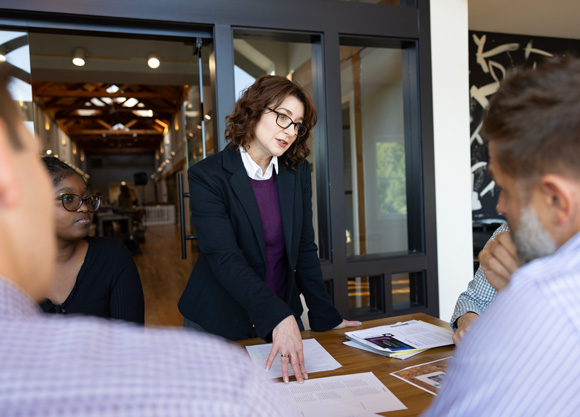 A woman speaking to 4 people at a conference table