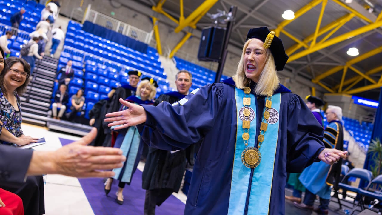 Marie Hardin high fives seated guests as she walks into the Inauguration ceremony