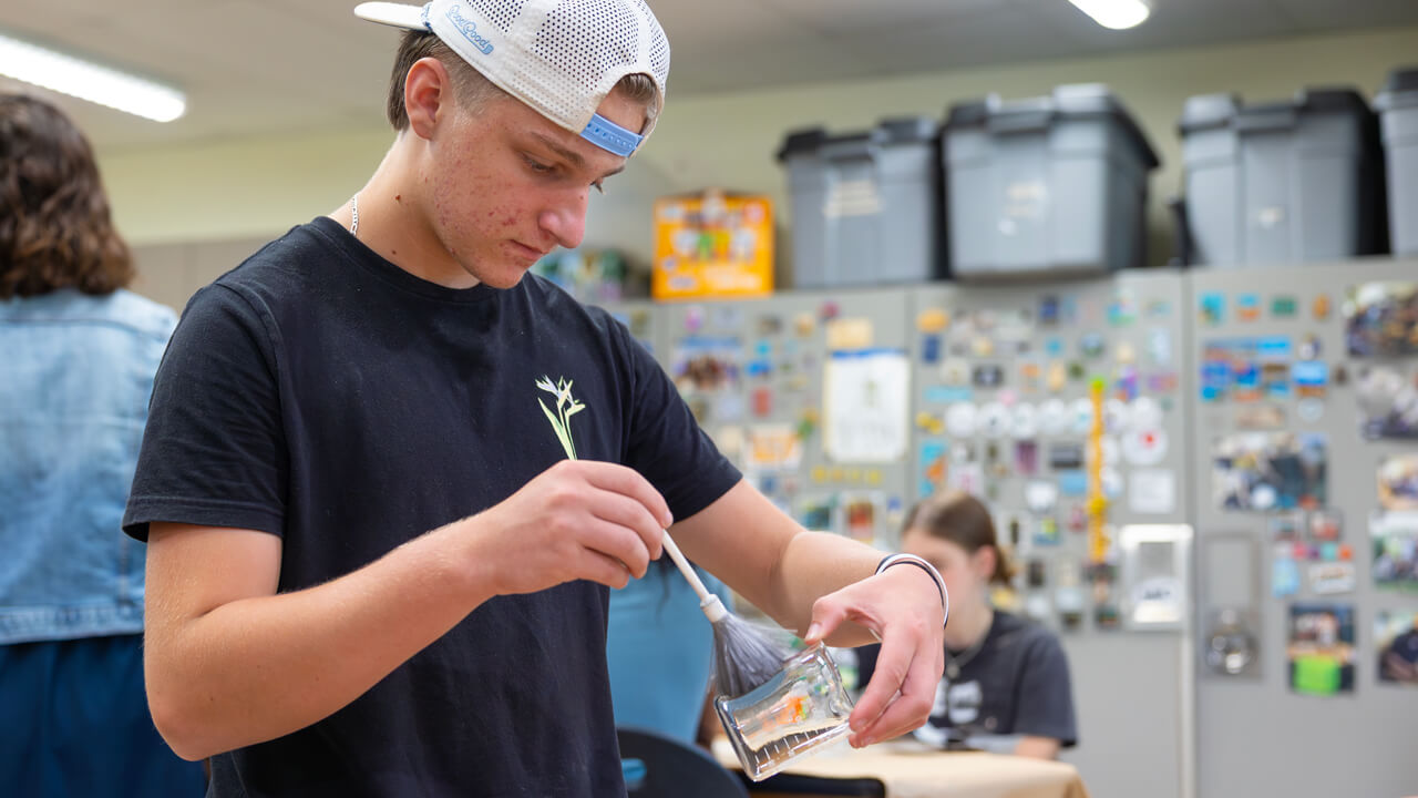 A high school student carefully dusts a glass beaker for fingerprints as part of a hands-on forensic science lab at Quinnipiac University.