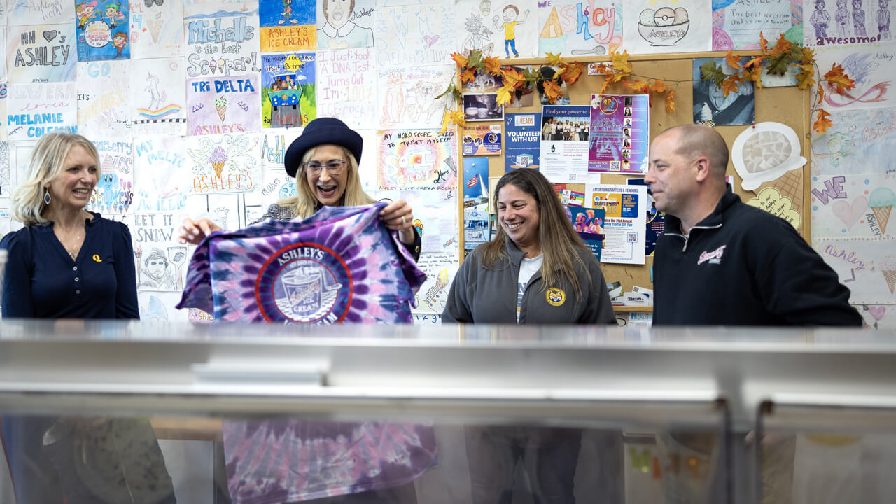 Marie Hardin holds up a bright tie dye Ashley's Ice Cream tee shirt while staff look on