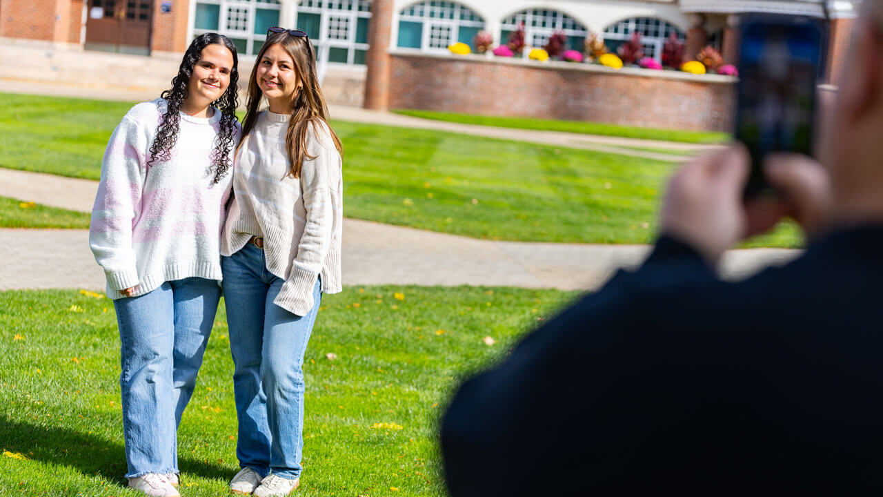 Two friends posing for a photo smiling in front of the Arnold Bernhard Library