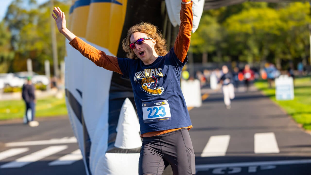 Runner with Quinnipiac shirt runs through Bobcat head with hands up