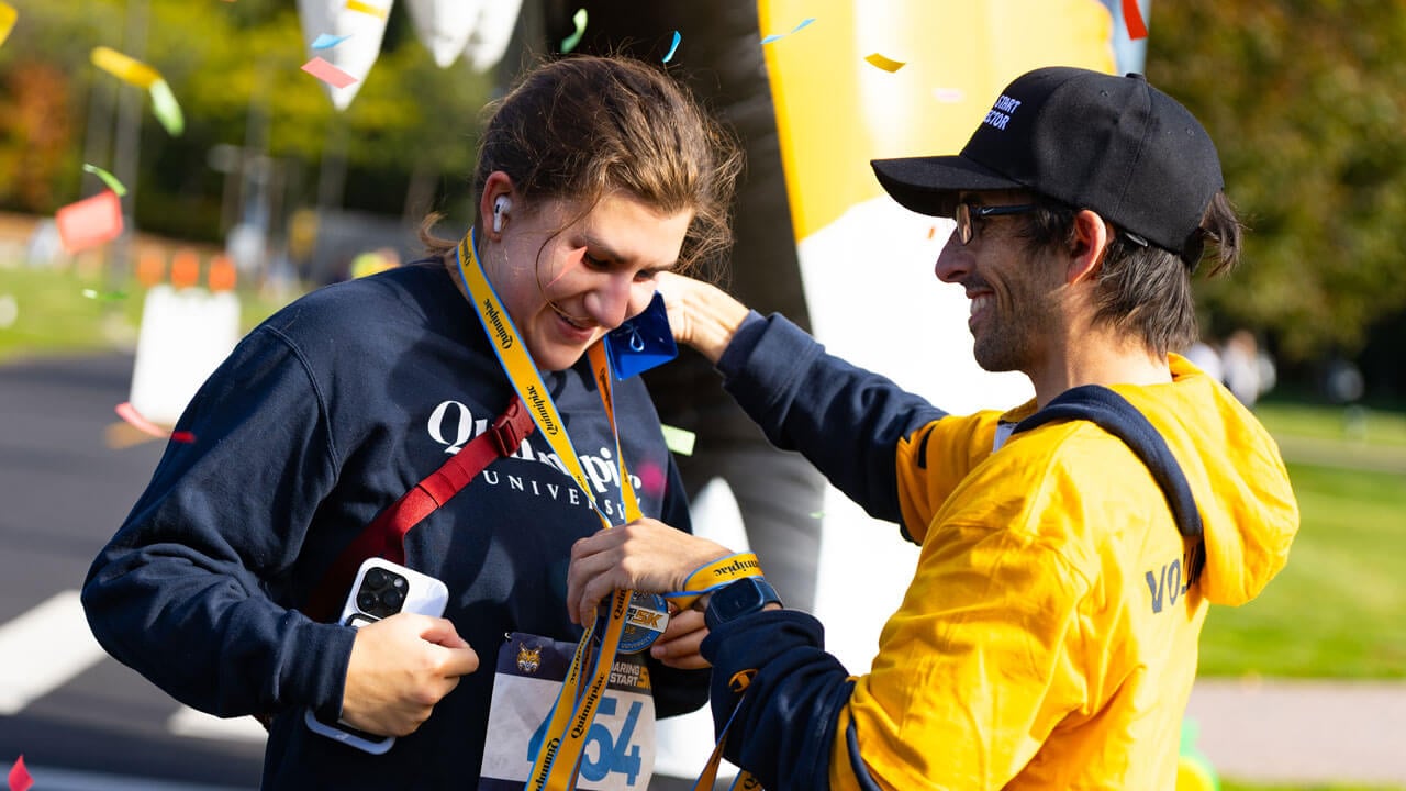 Jamie Deloma awarding a medal to Jackie Ydrovo after completing the race with confetti in background