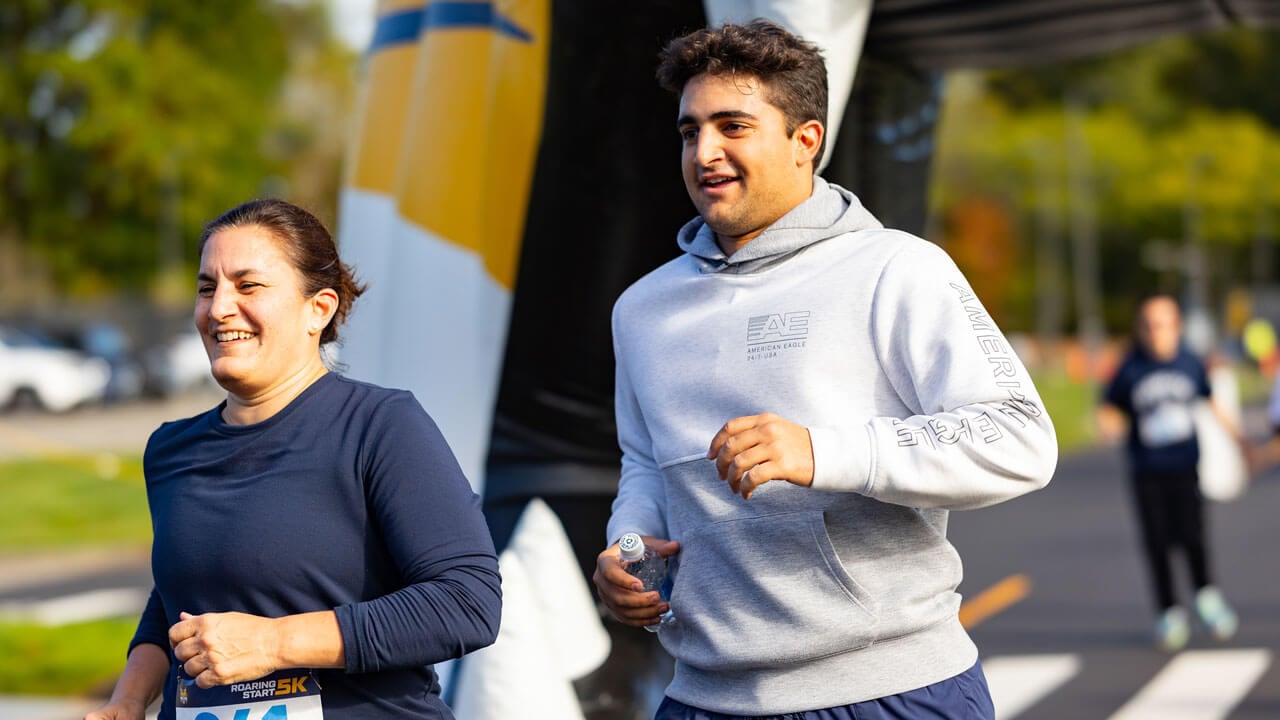 Two runners with prideful smiles as they run through the Bobcat head to finish the 5K