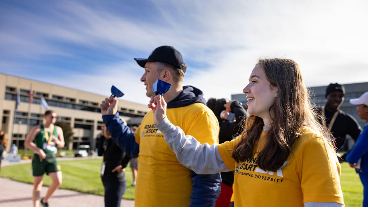 Two student volunteers cheering on the runners with cowbells