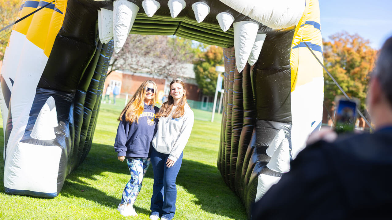 Two friends smile in front of an inflatable bobcat