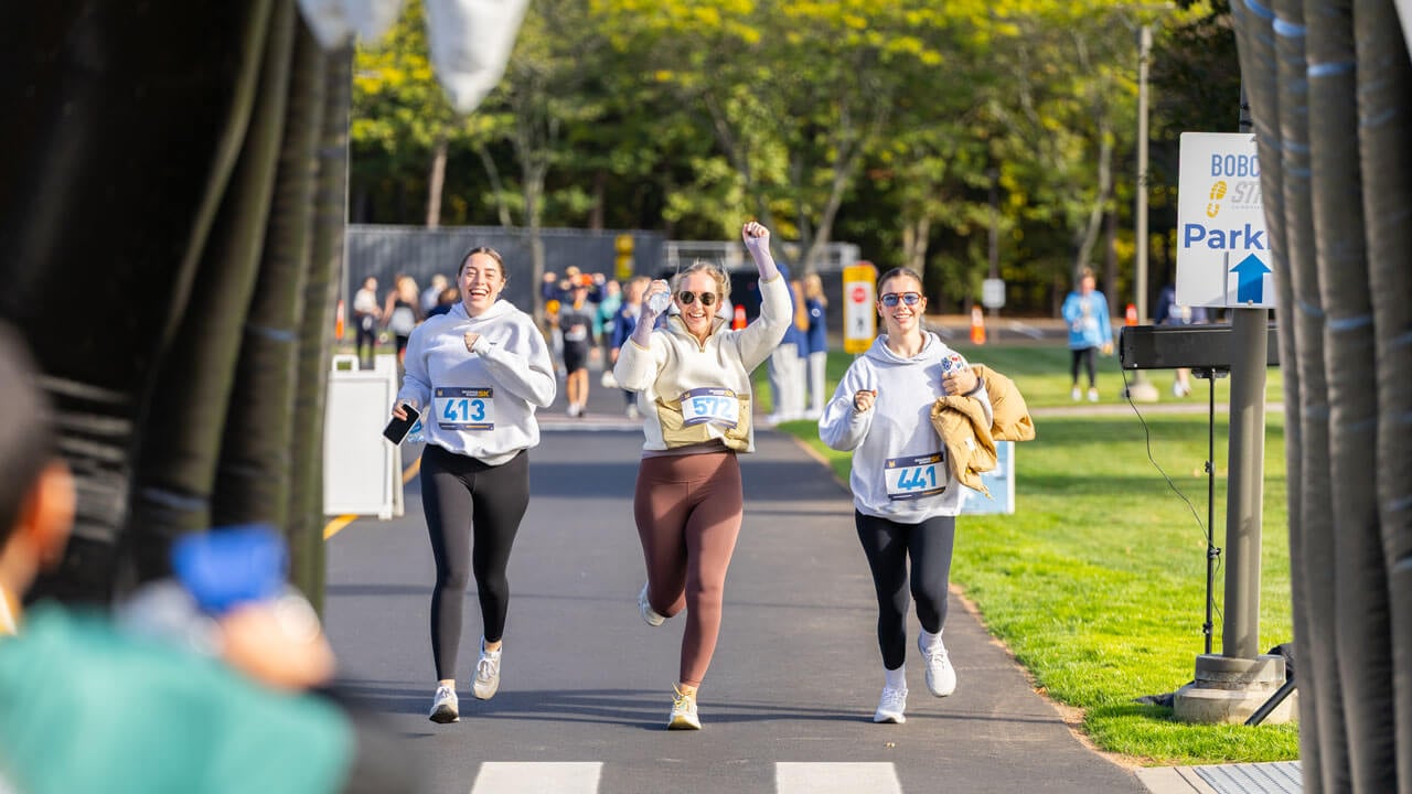 Three runners with smiles during the race with one runner with their hands up in the middle