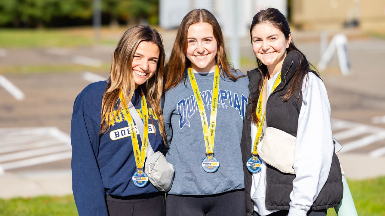 Three students smile for a photo with medals over their necks after running the 5K
