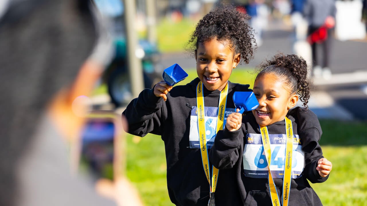 Two smiling children with medals around their necks and cowbells in hand
