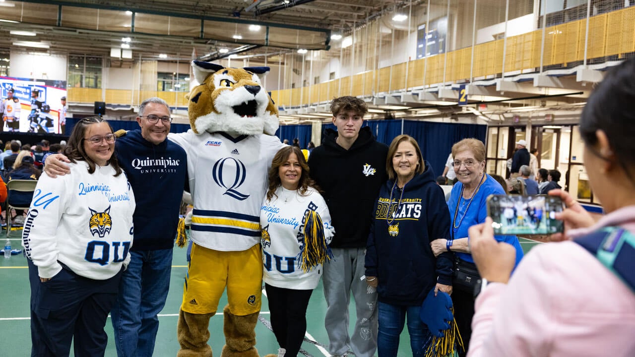 Family with Quinnipiac gear on pose for a photo with Boomer the Bobcat