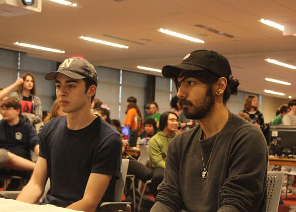 Two men sit at a desk playing esports.