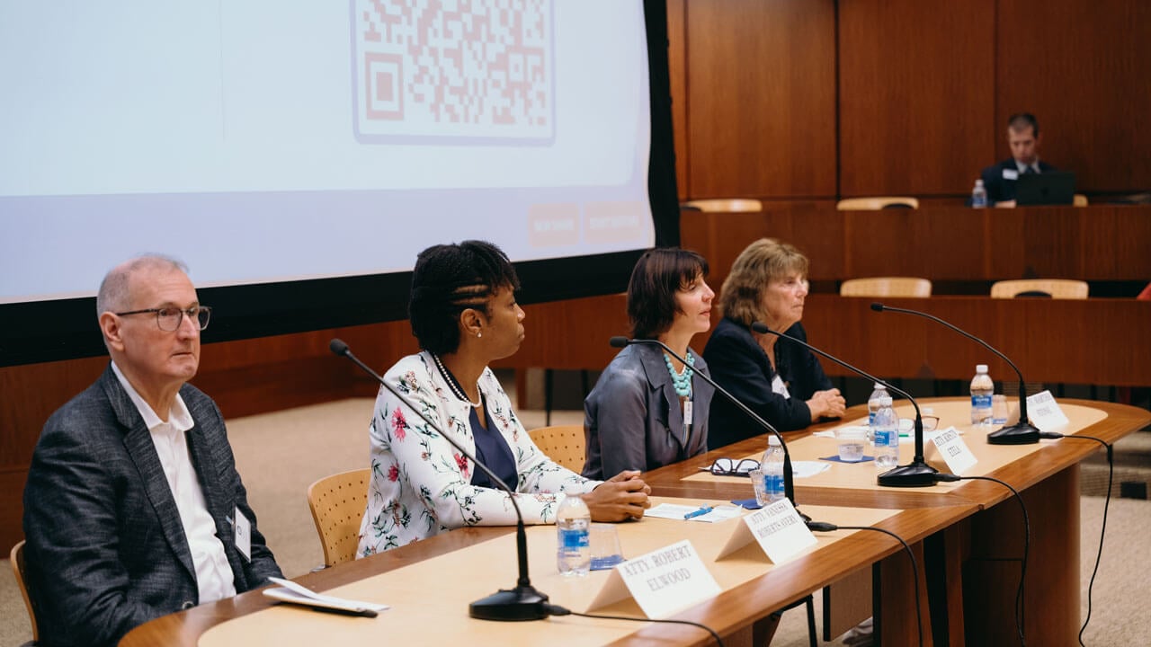 Panel of speakers sits at a table while looking out to a crowd