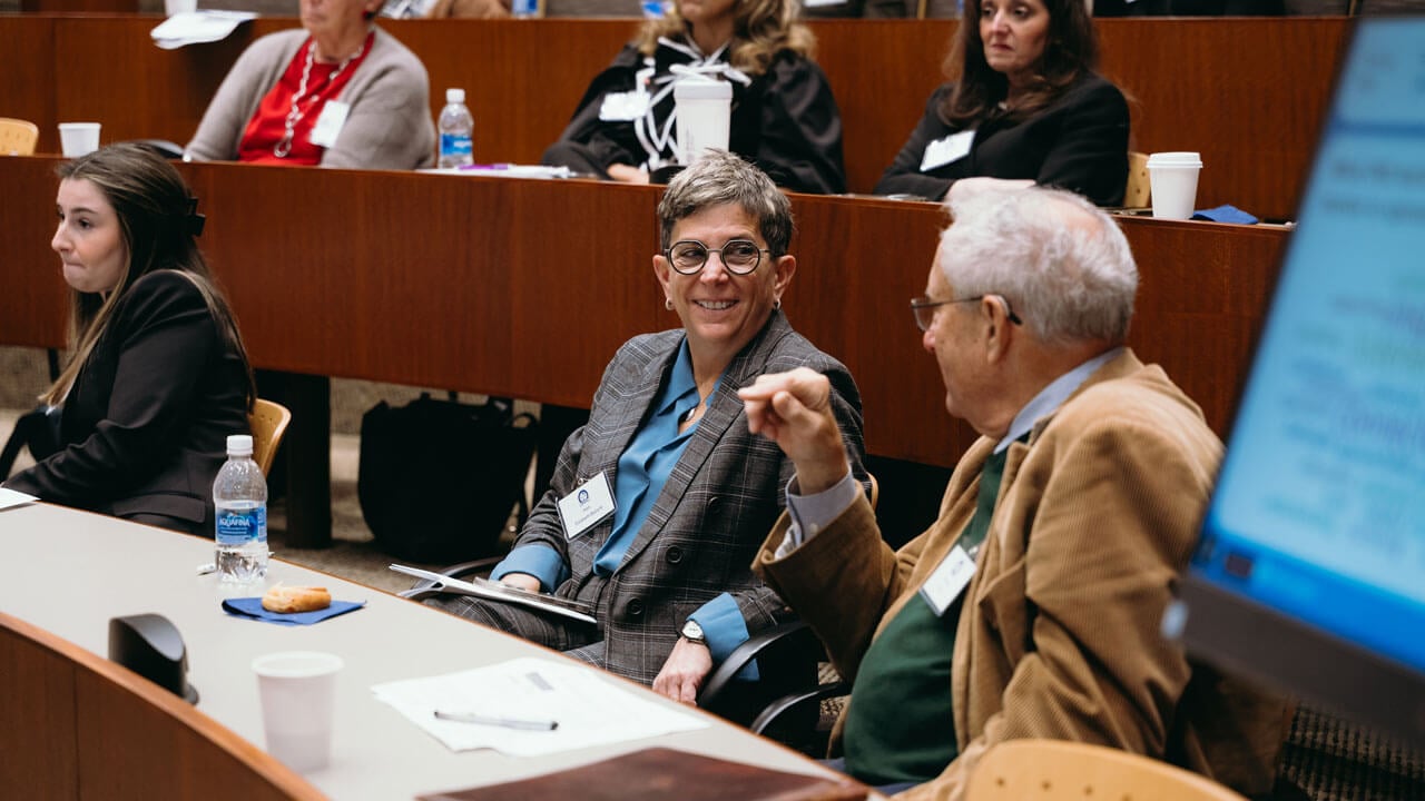 Two audience members sit and talk to each other while smiling