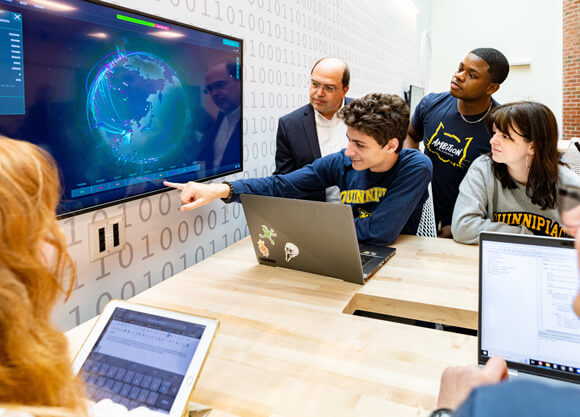 A group of students at a table looking at a screen with a 3D globe with a professor looking over their shoulder