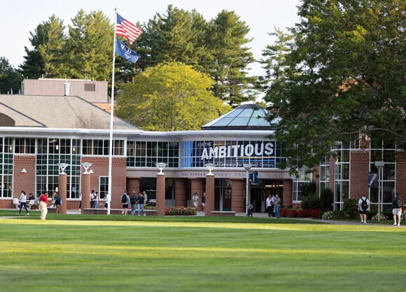 People walk in and out of the Quinnipiac student center with For the Ambitious logo in the windows