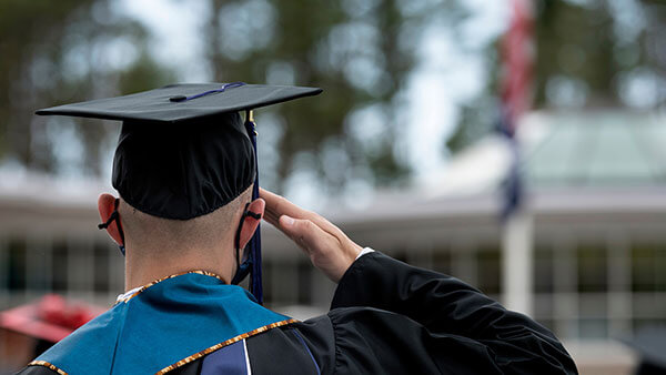 Graduate in cap and gown saluting the American flag.