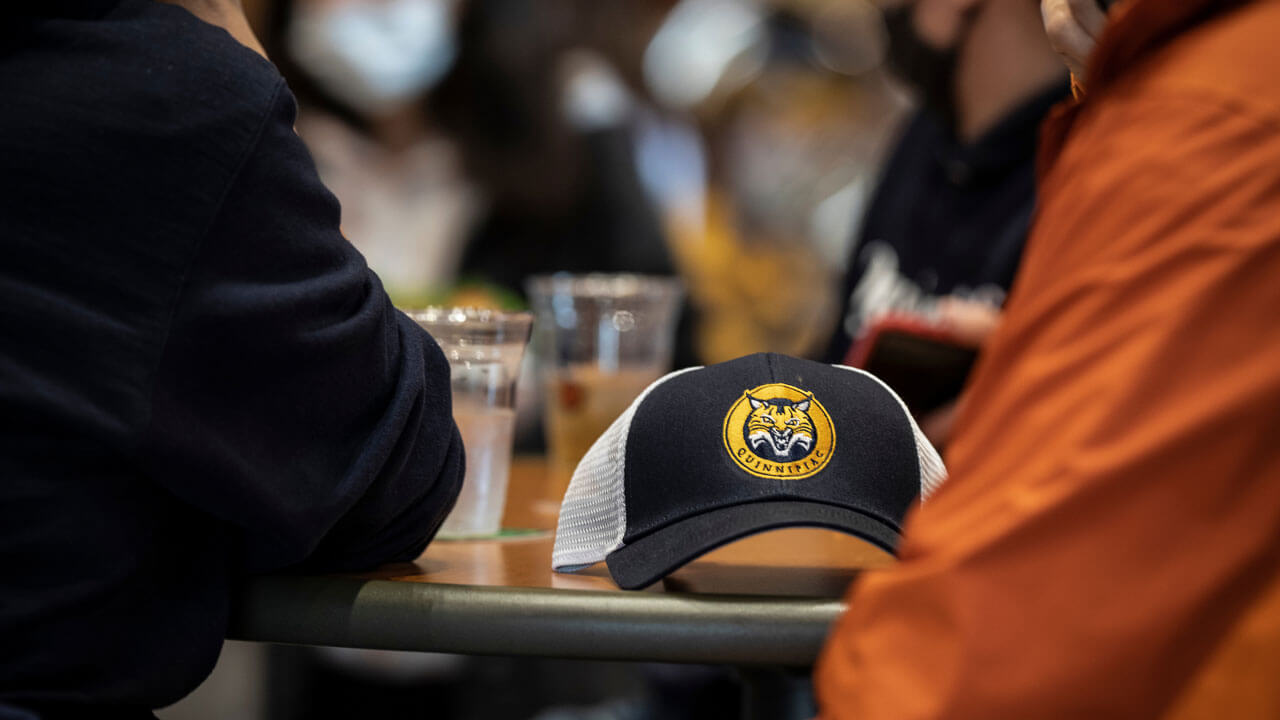 Bobcat cap on table surrounded by people at on the rocks