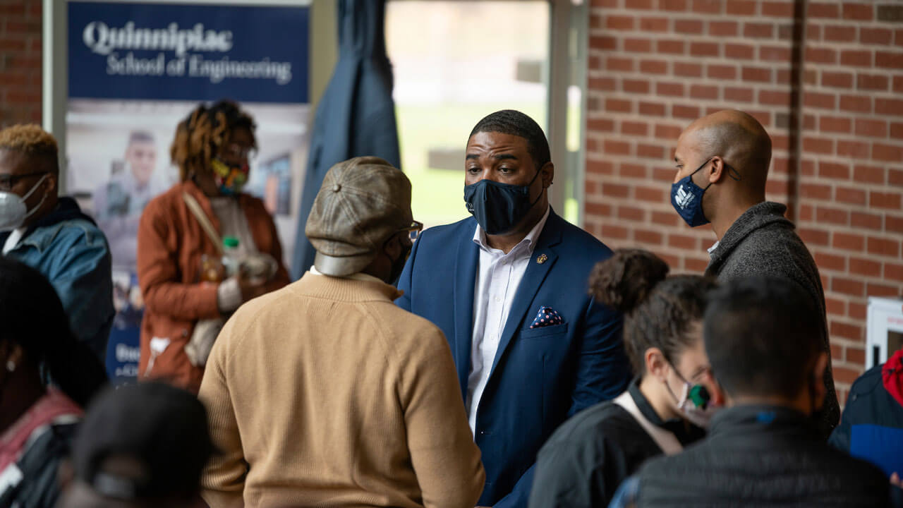 People gathered and talking at a table in CCE in front of a school of engineering sign