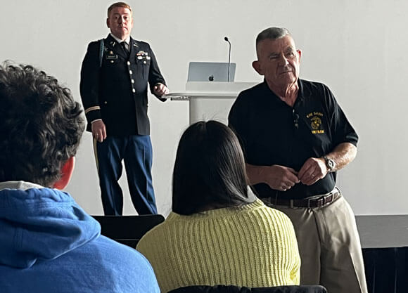 An audience looks up to veterans speaking at the front of a room
