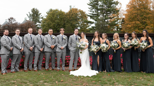 Julia Basso and Cameron Mowry smile with their wedding party in front of a Quinnipiac sign