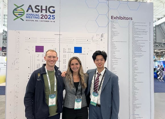 Three Quinnipiac School of Medicine students stand in front of an American Society of Human Genetics (ASHG) Conferencesign