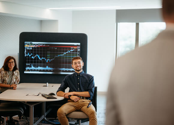 Two students seated at a table next to a statistical graph, smiling at a professor shown from behind.