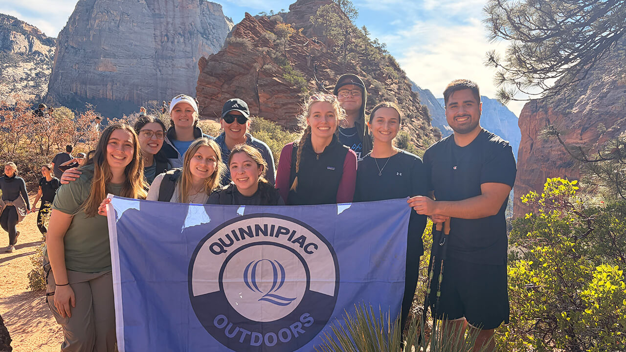 Students hold Quinnipiac Outdoors flag in Utah