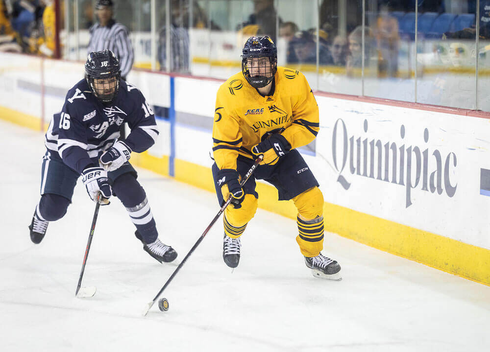 A Quinnipiac men's hockey player skates with the puck on home ice
