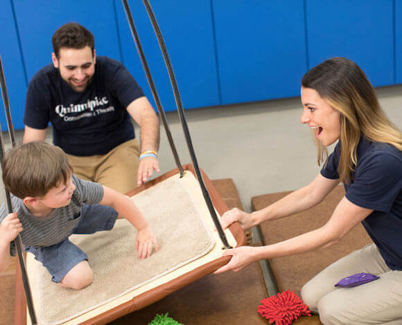 Two occupational therapy students work with a child on a swing board in the movement lab.