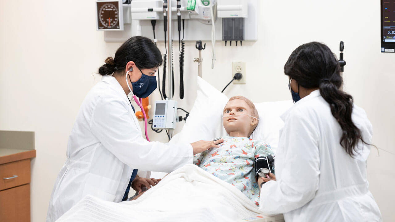 Two accelerated nursing students practice clinical skills with a mannequin