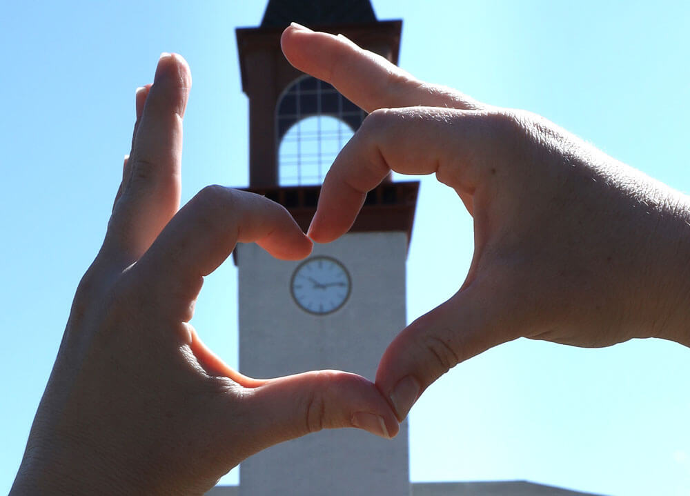A student forms her hand into a heart with the Quinnipiac clocktower in the background