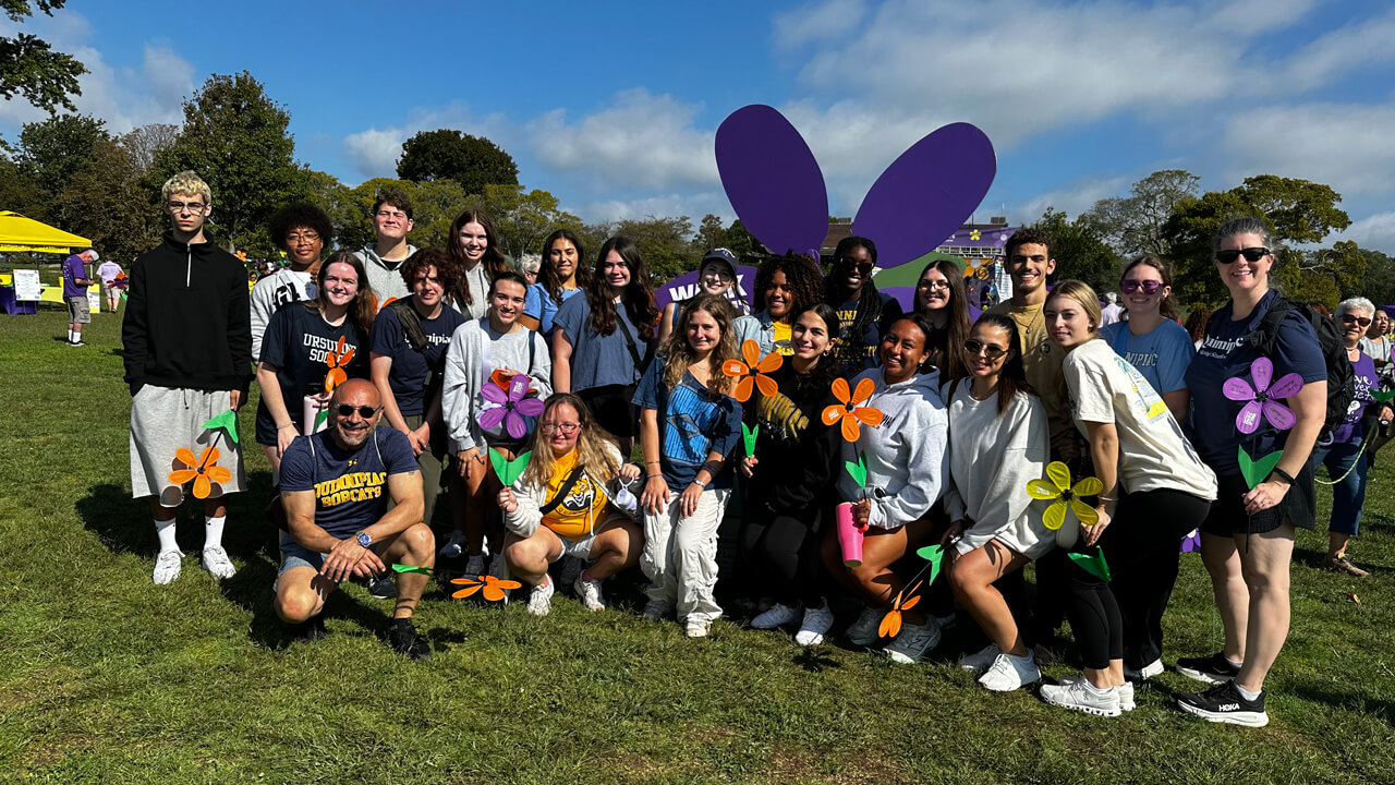 A group of about 20 students standing outside on a sunny day, holding flower decorations.
