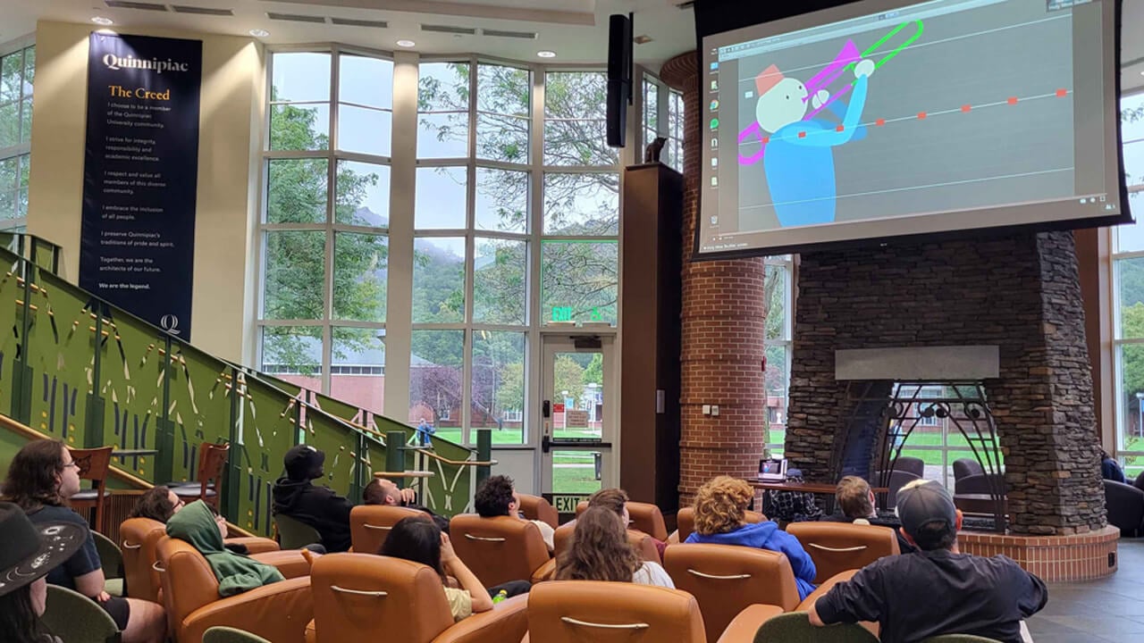 Students sitting in comfy chairs looking up at a projector screen with a video game on it